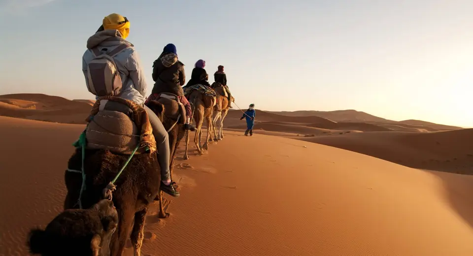 A camel caravan crossing the dunes at sunset