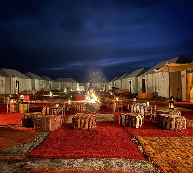 A desert camp at night, rugs and lanterns around a fire