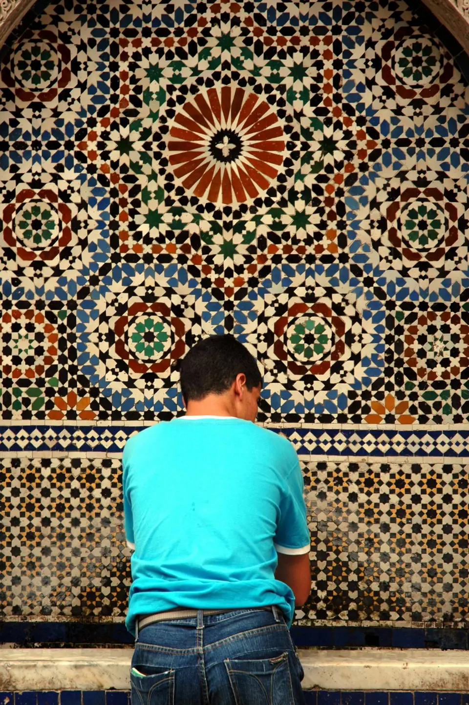 A man seated before a zellige mosaic wall
